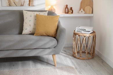 Different soft pillows on gray sofa and side table with books in living room