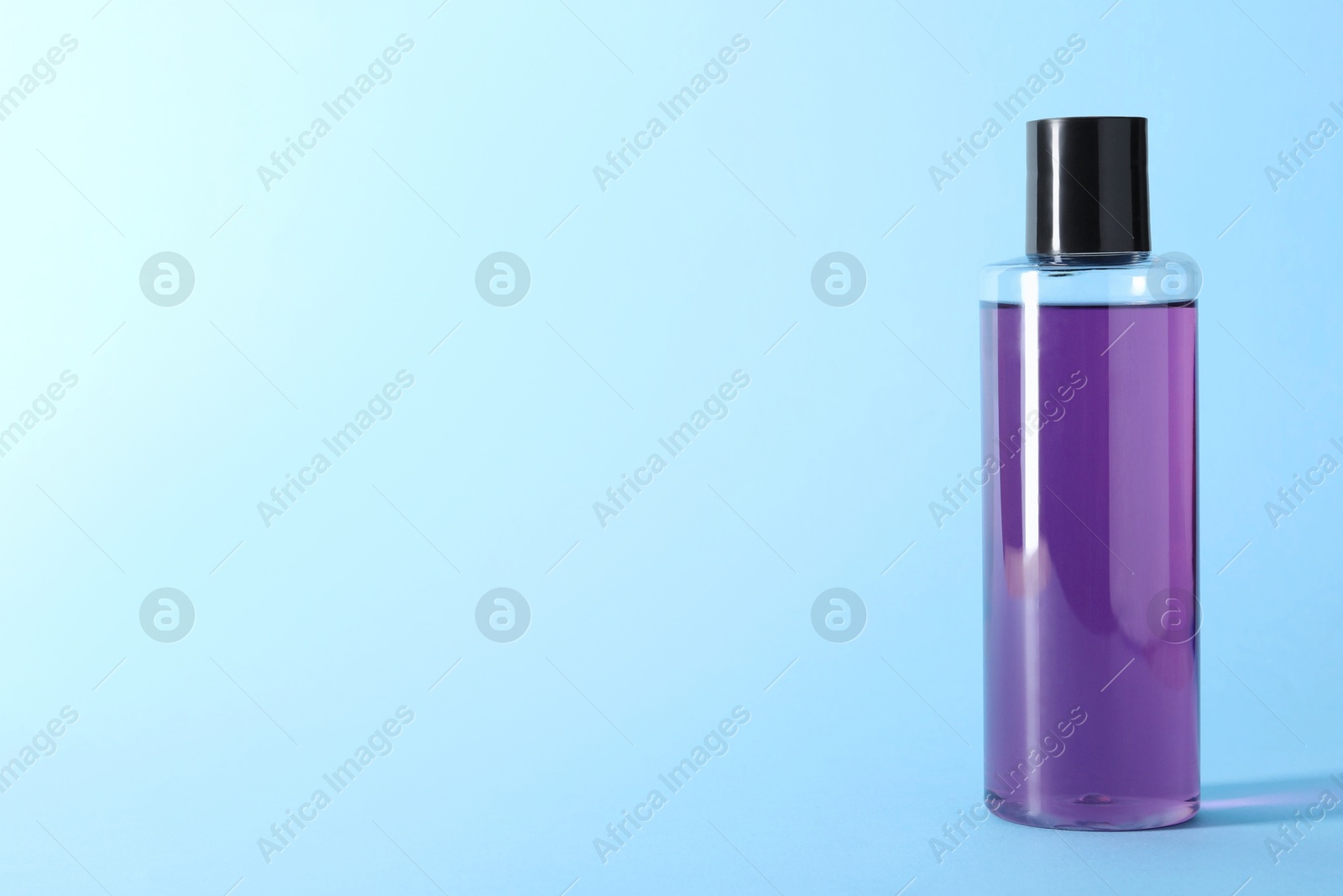 Photo of Shampoo in bottle on light blue background, space for text