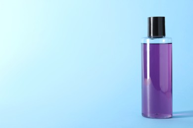 Photo of Shampoo in bottle on light blue background, space for text