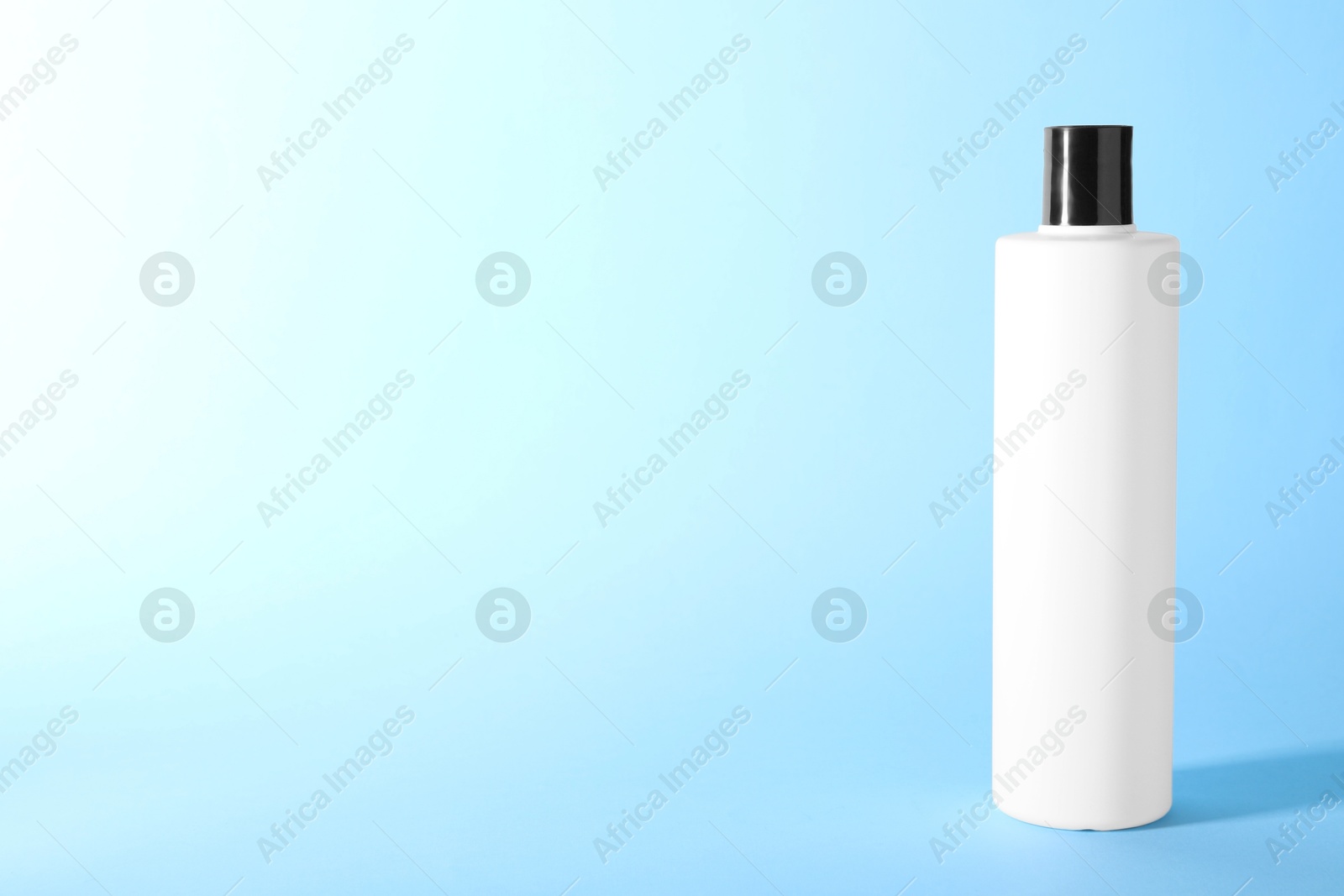 Photo of Shampoo in bottle on light blue background, space for text