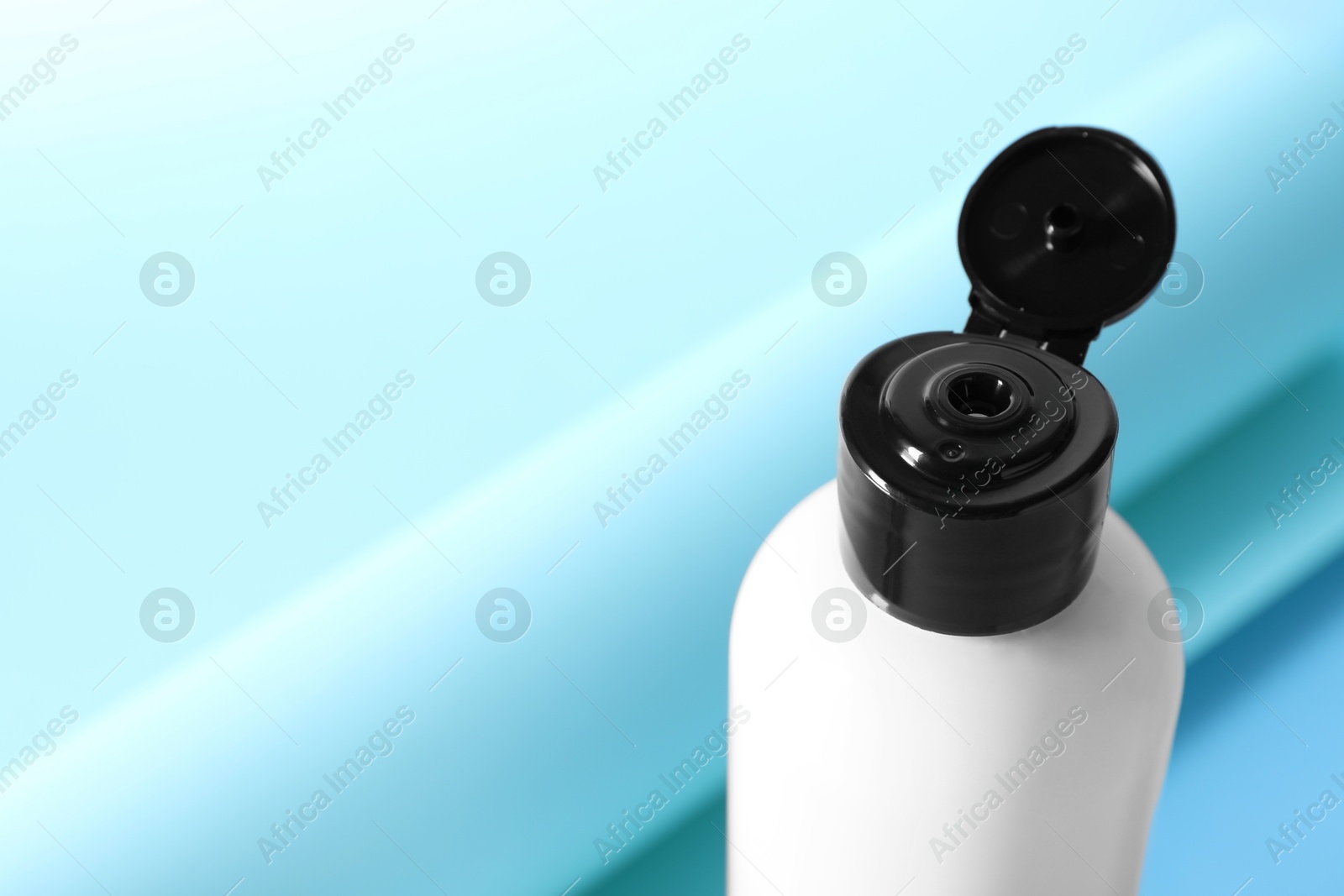 Photo of Shampoo in bottle on light blue background, closeup. Space for text