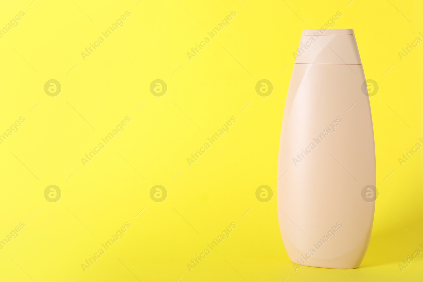 Photo of Shampoo in container on yellow background, space for text