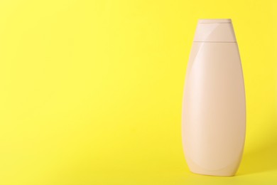 Photo of Shampoo in container on yellow background, space for text