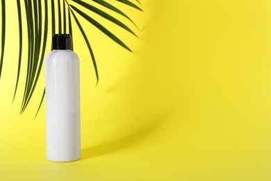 Photo of Shampoo in bottle and green palm leaves on yellow background. Space for text