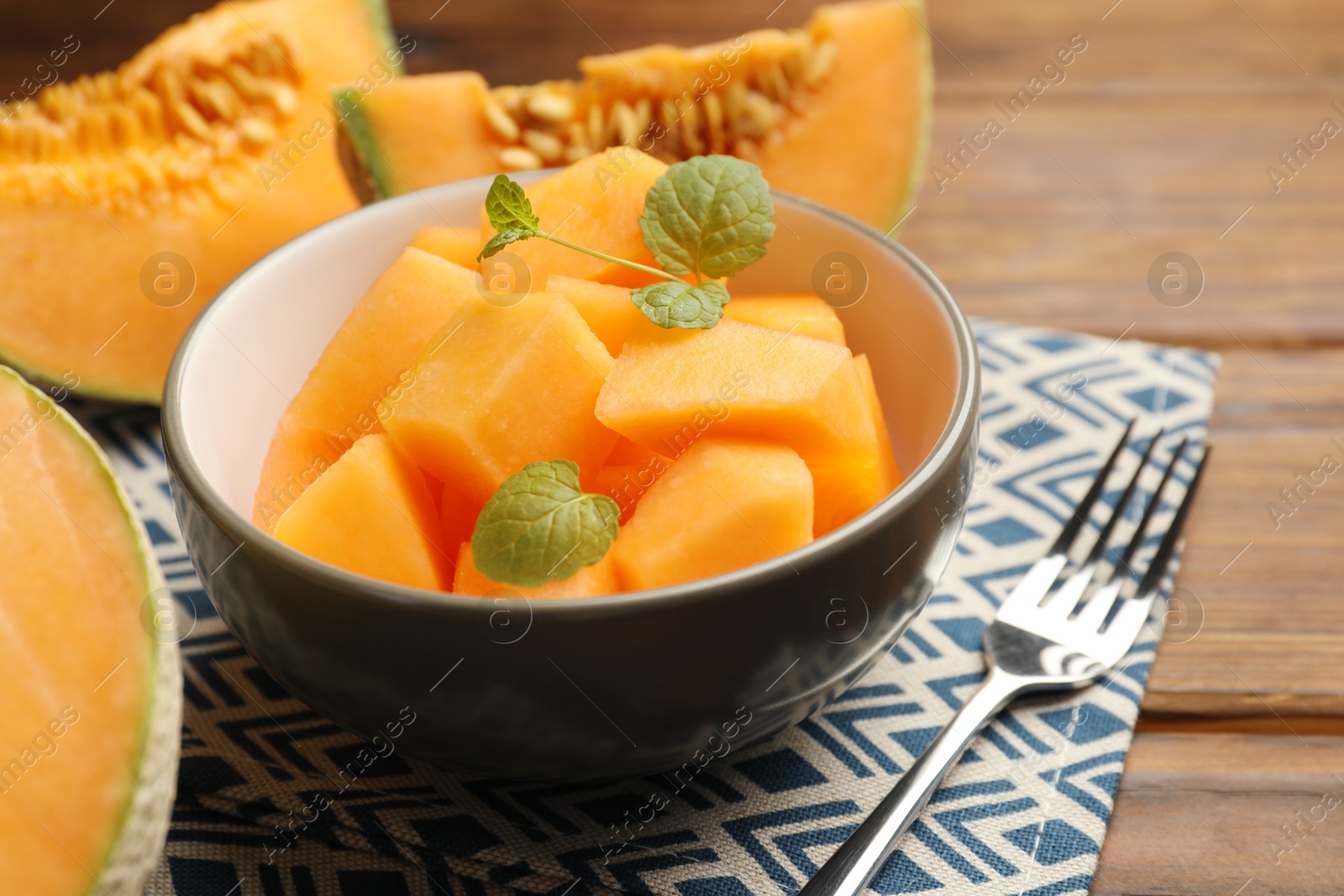 Photo of Pieces of ripe Cantaloupe melon in bowl and fork on wooden table, closeup