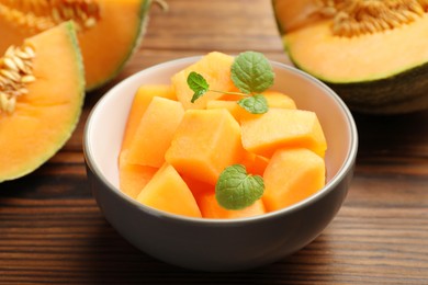 Photo of Pieces of Cantaloupe melon and mint in bowl on wooden table, closeup