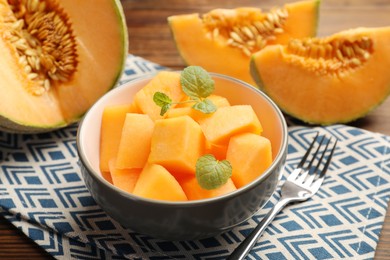 Photo of Pieces of ripe Cantaloupe melon in bowl and fork on table, closeup