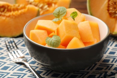 Photo of Pieces of ripe Cantaloupe melon in bowl and fork on table, closeup