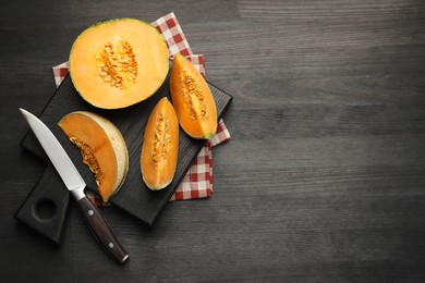 Photo of Fresh ripe Cantaloupe melon and knife on dark wooden table, flat lay. Space for text