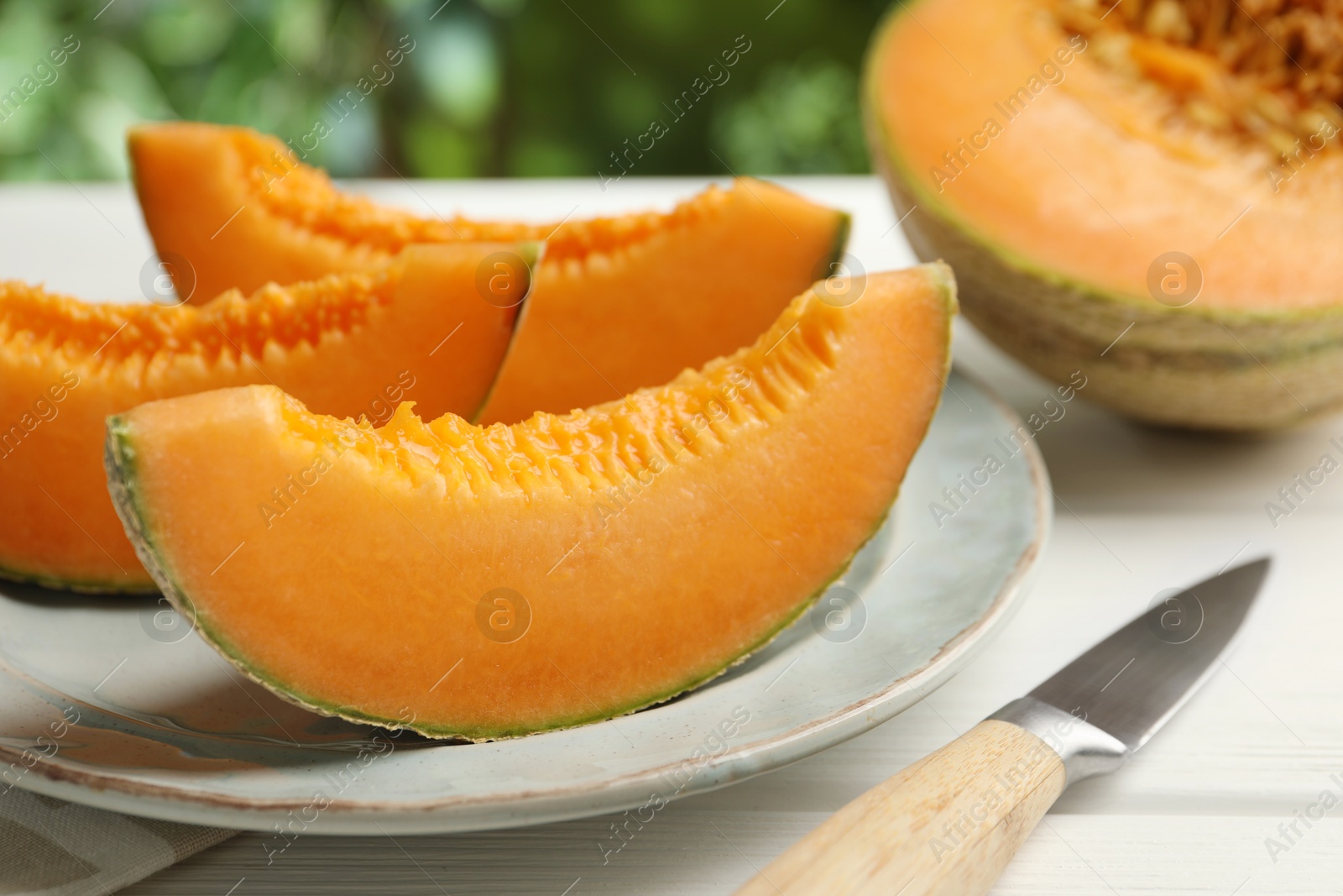 Photo of Pieces of fresh Cantaloupe melon and knife on white wooden table, closeup