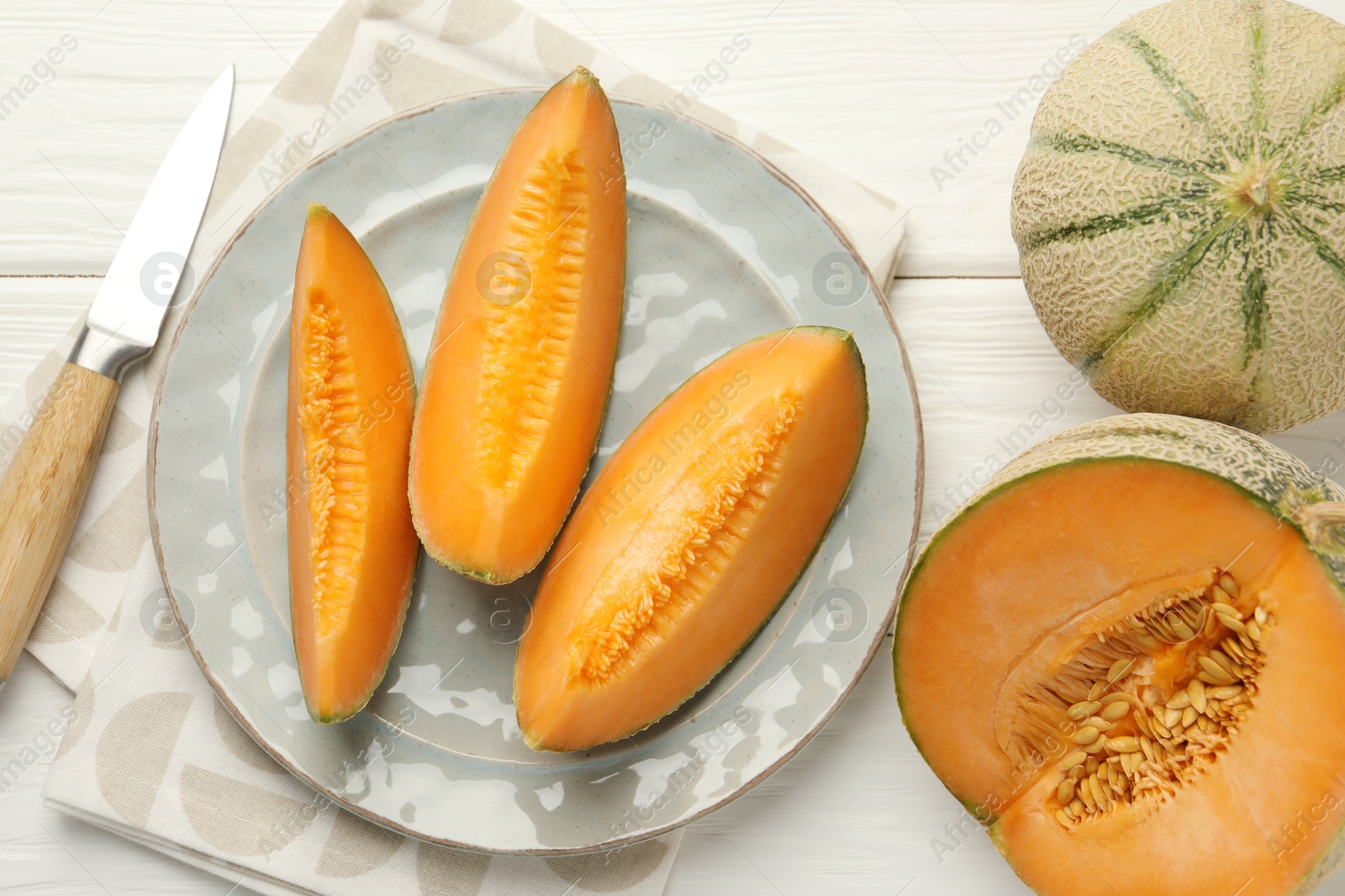 Photo of Tasty ripe Cantaloupe melons and knife on white wooden table, flat lay