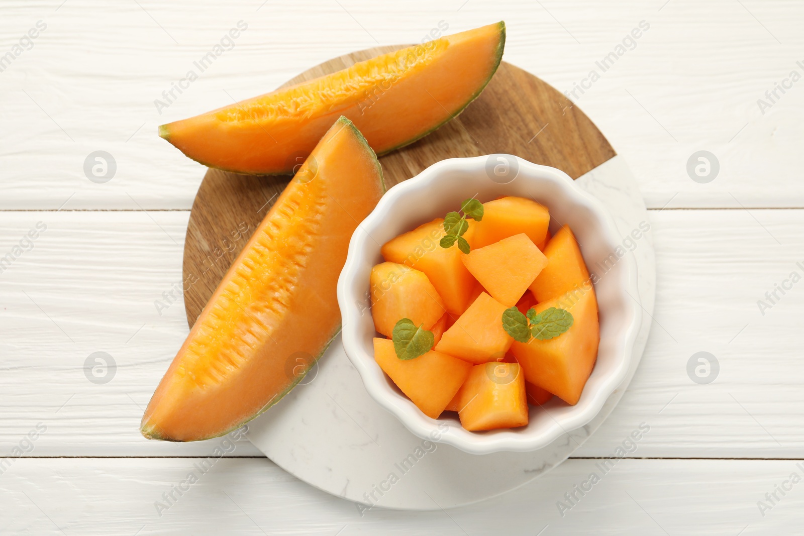 Photo of Pieces of Cantaloupe melon and mint in bowl on white wooden table, top view