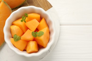 Photo of Pieces of Cantaloupe melon and mint in bowl on white wooden table, top view. Space for text