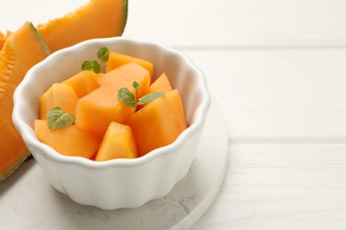 Photo of Pieces of Cantaloupe melon and mint in bowl on white wooden table, closeup