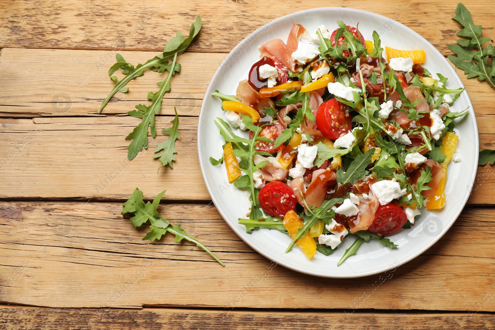 Photo of Tasty salad with arugula, cheese and vegetables on wooden table, flat lay. Space for text