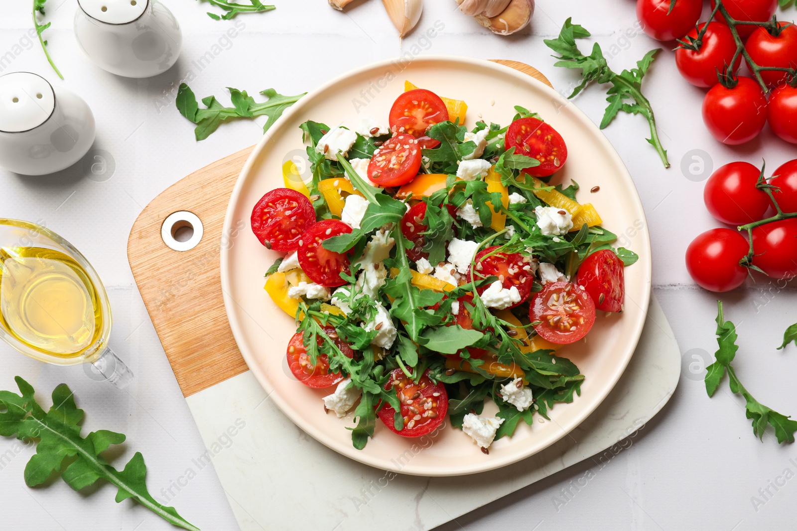 Photo of Tasty salad with arugula, cheese and vegetables on white tiled table, flat lay