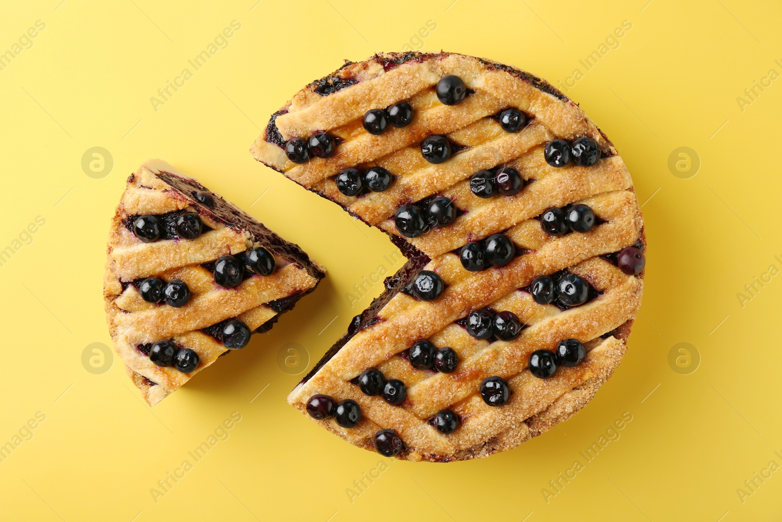 Photo of Cut homemade blueberry pie on yellow background, top view