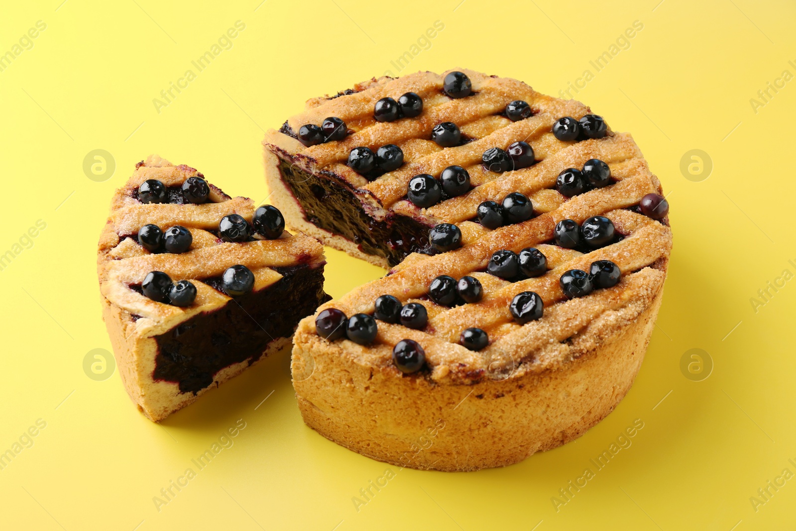 Photo of Cut homemade blueberry pie on yellow background