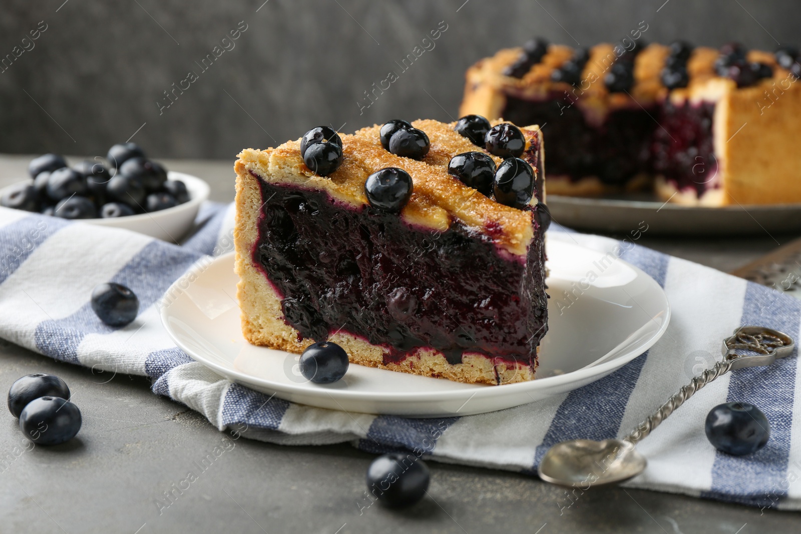 Photo of Slice of delicious homemade blueberry pie served on grey table, closeup