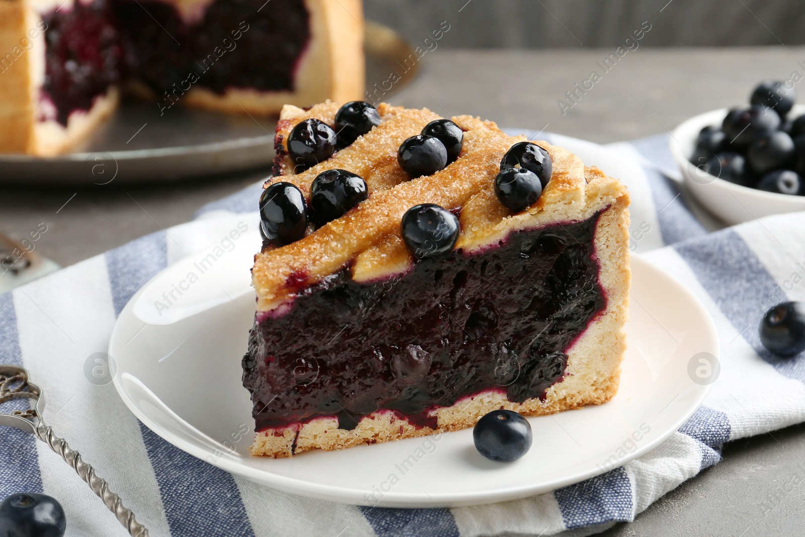 Photo of Slice of delicious homemade blueberry pie served on grey table, closeup