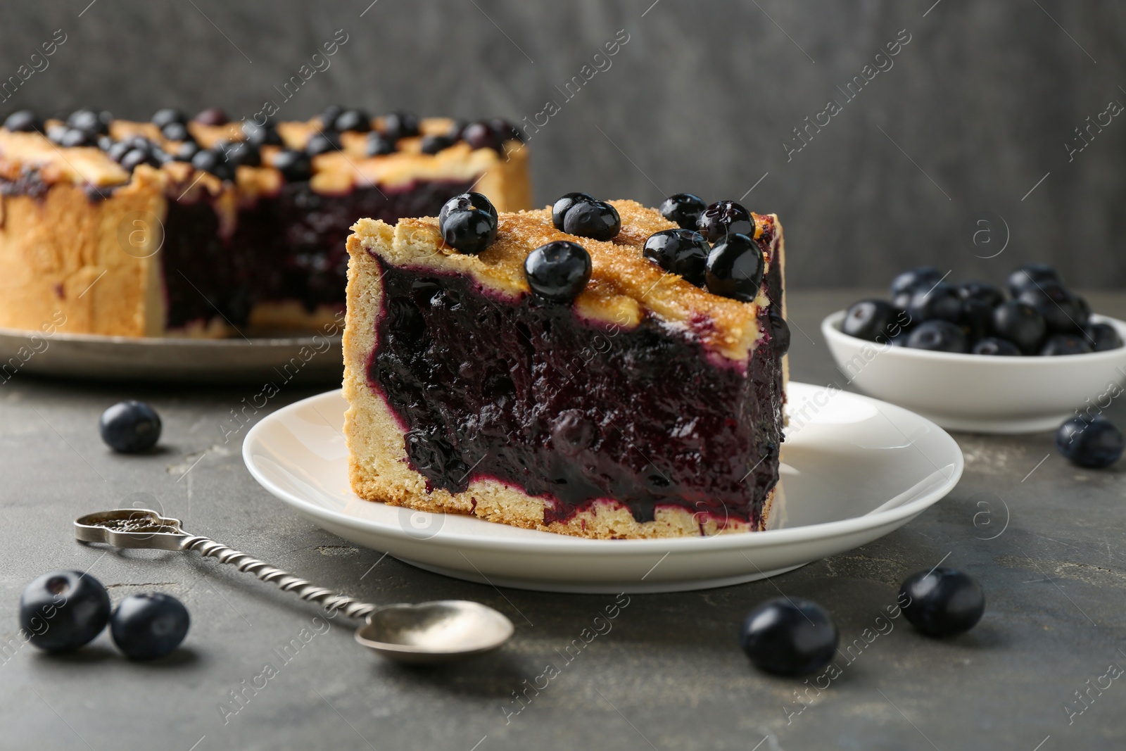 Photo of Slice of delicious homemade blueberry pie served on grey table, closeup