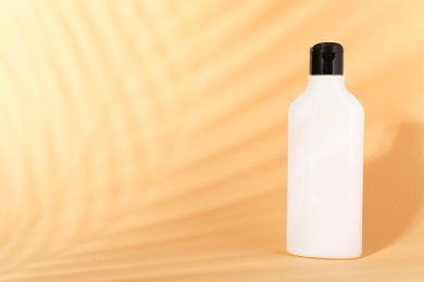 Shampoo in bottle on pale orange background, space for text