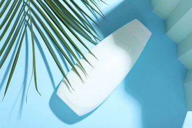 Shampoo in bottle and palm leaf on light blue background, top view