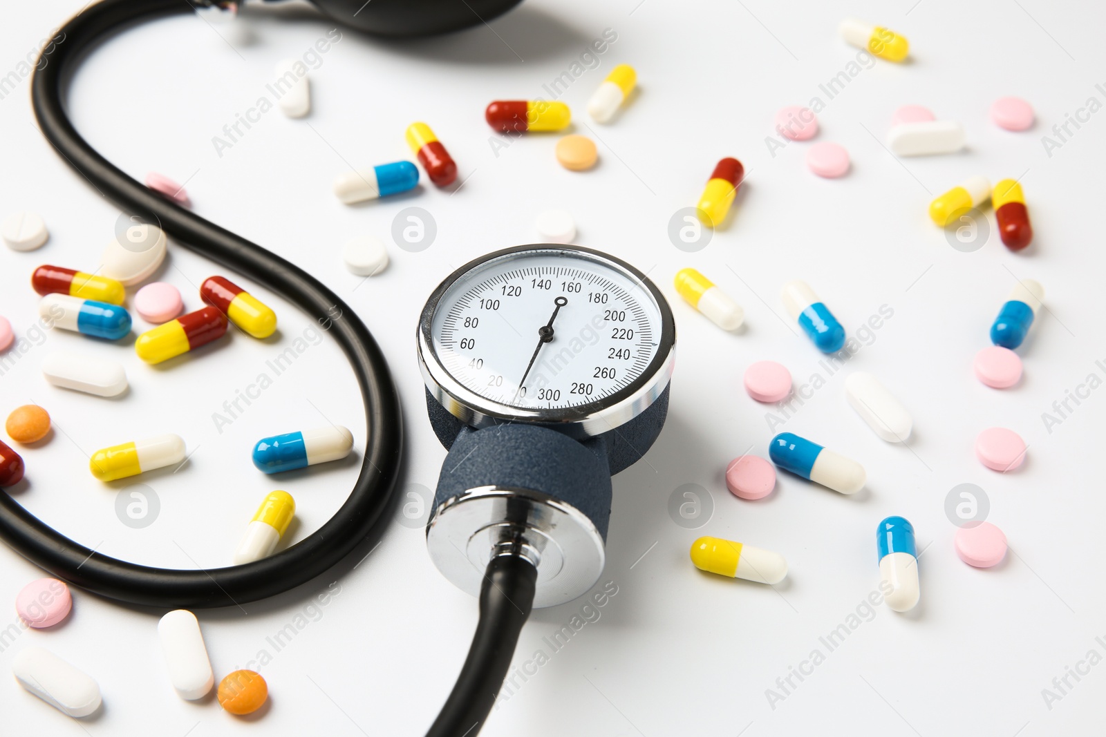 Photo of Blood pressure measuring device and pills on white background, closeup