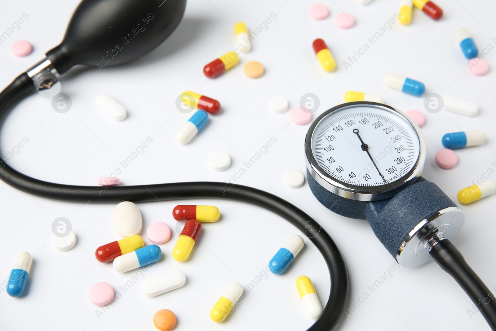 Photo of Blood pressure measuring device and pills on white background, closeup