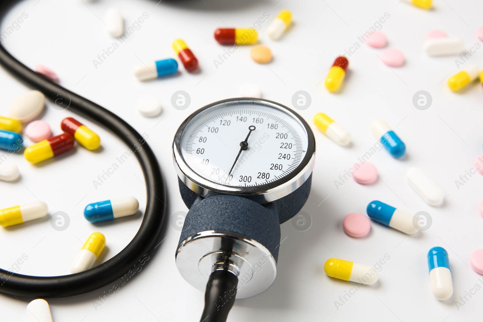 Photo of Blood pressure measuring device and pills on white background, closeup