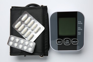 Blood pressure measuring device and pills on white background, top view