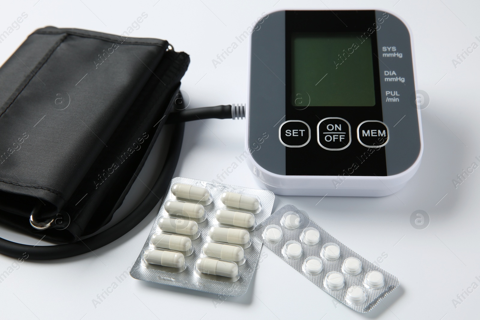 Photo of Blood pressure measuring device and pills on white background, closeup