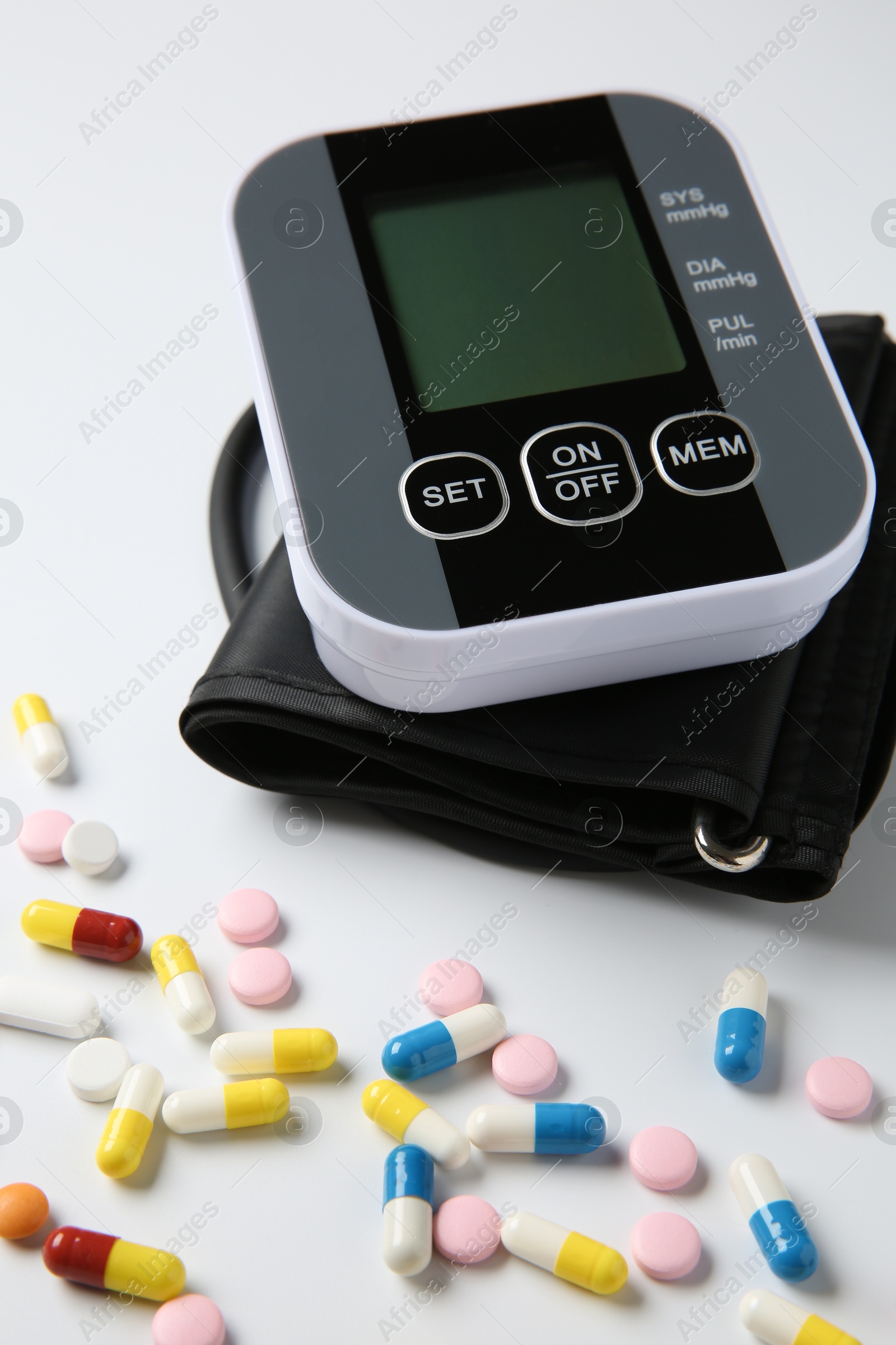 Photo of Blood pressure measuring device and pills on white background, closeup