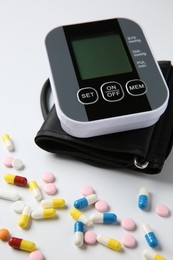 Blood pressure measuring device and pills on white background, closeup