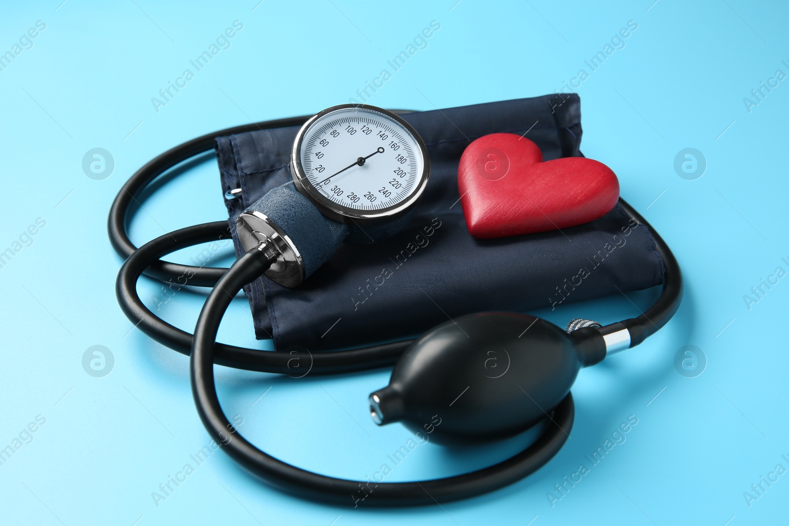 Photo of Blood pressure measuring device and heart figure on light blue background, closeup