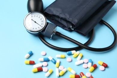 Photo of Blood pressure measuring device and pills on light blue background, closeup