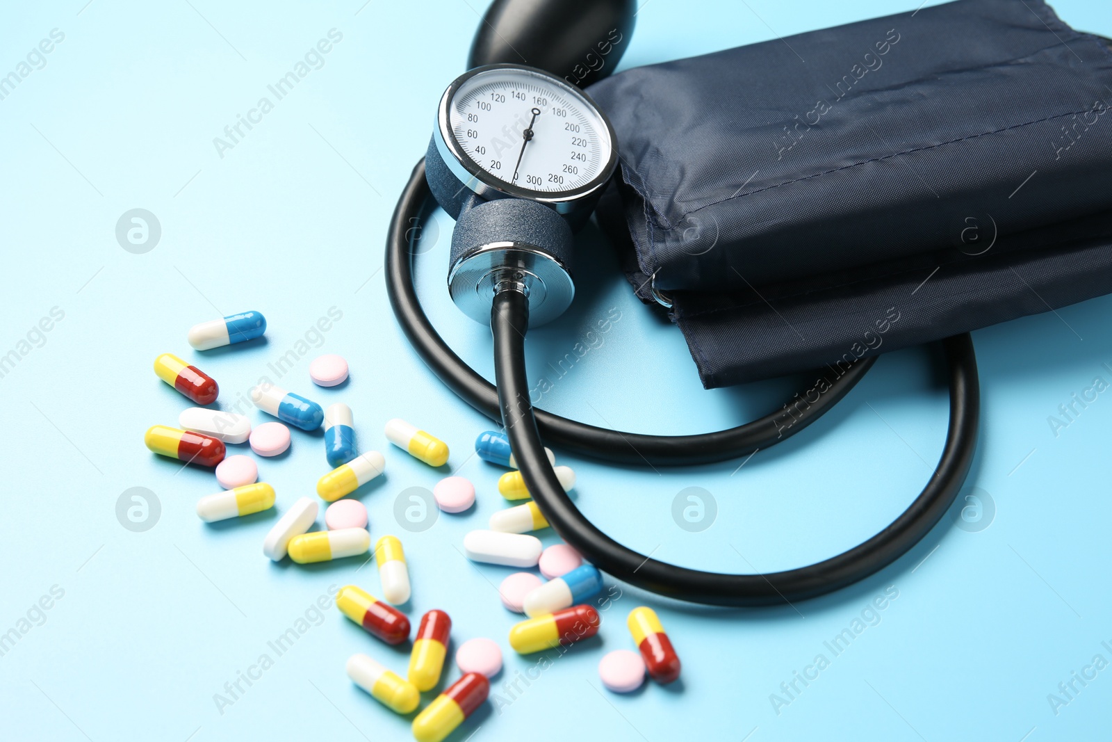 Photo of Blood pressure measuring device and pills on light blue background, closeup