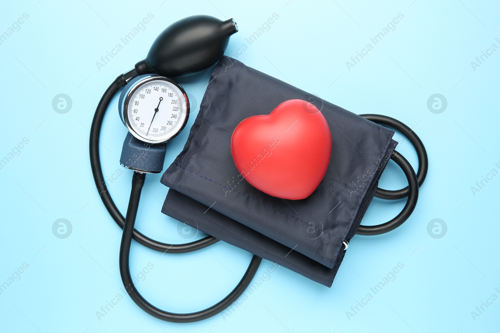 Photo of Blood pressure measuring device and squeeze heart on light blue background, top view