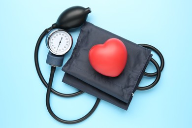 Blood pressure measuring device and squeeze heart on light blue background, top view