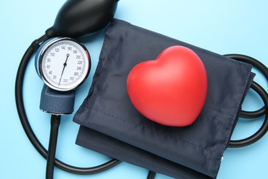 Photo of Blood pressure measuring device and squeeze heart on light blue background, top view