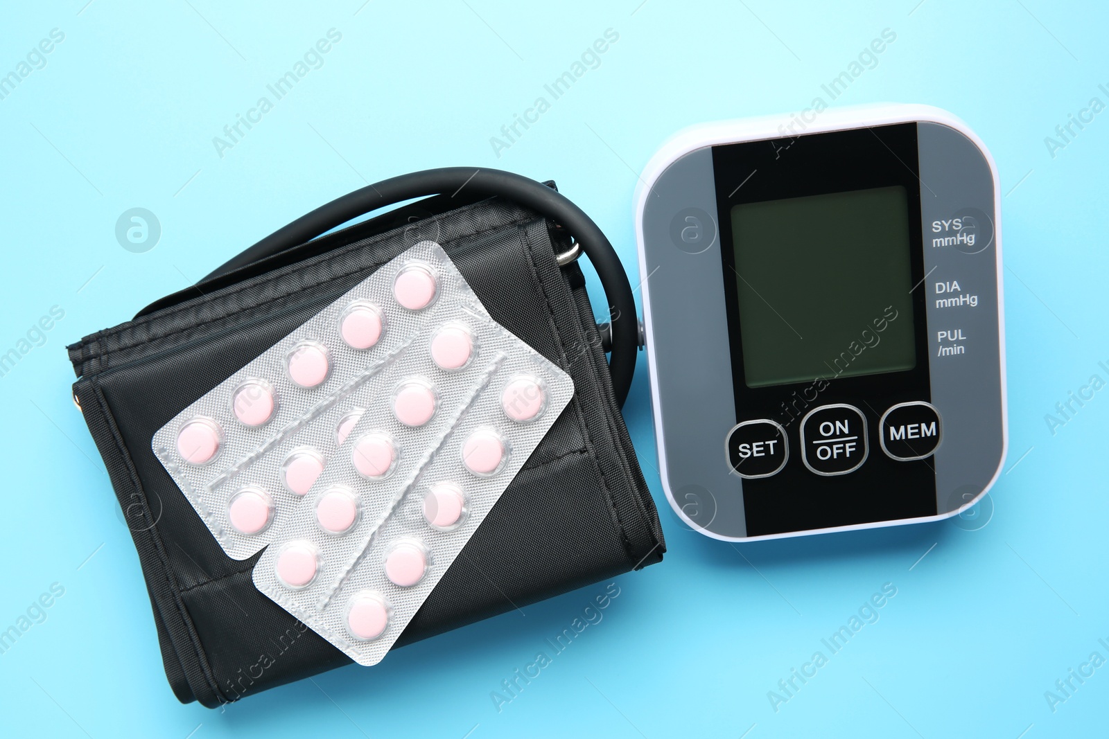 Photo of Blood pressure measuring device and pills on light blue background