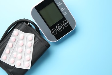 Photo of Blood pressure measuring device and pills on light blue background, top view. Space for text