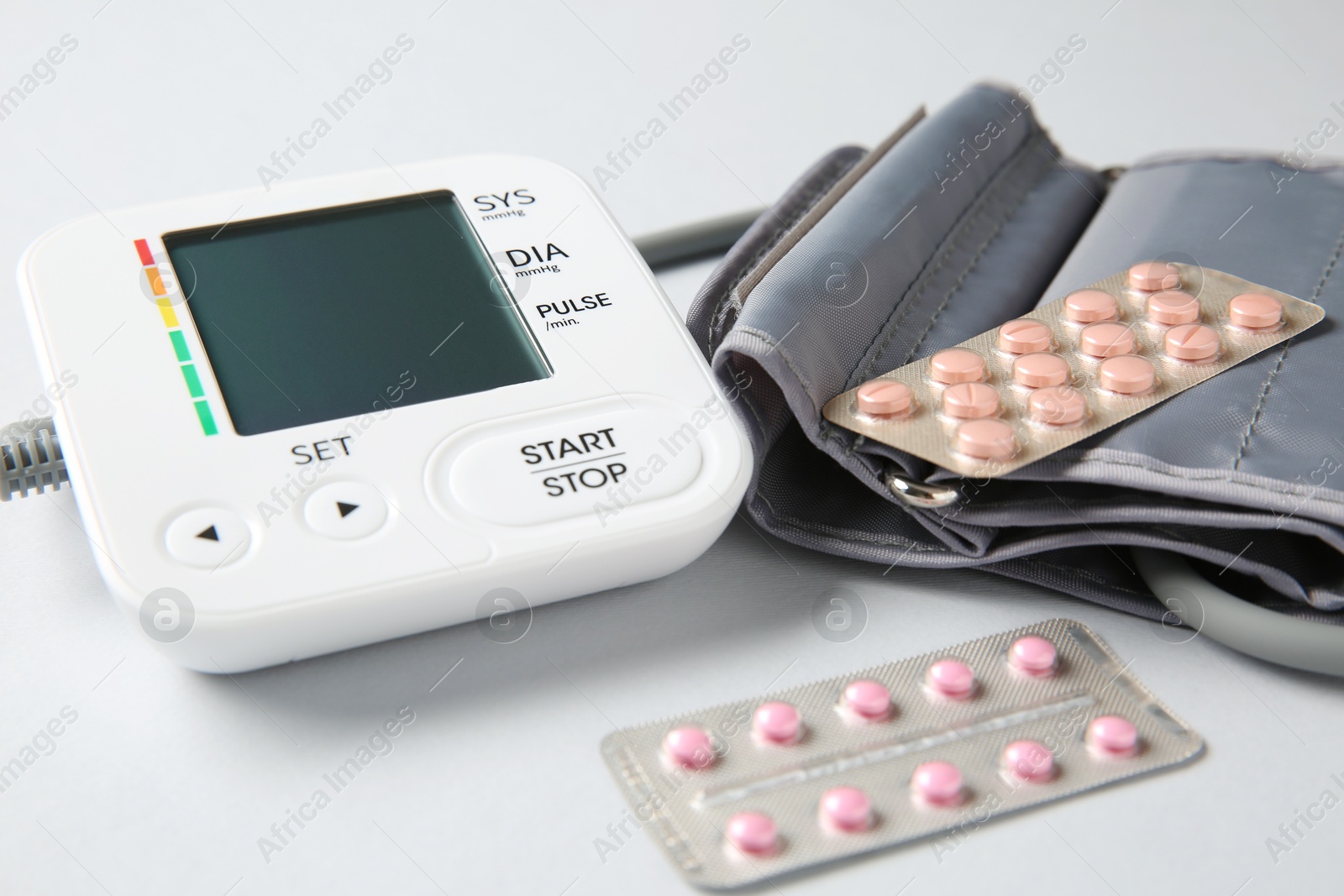 Photo of Blood pressure measuring device and pills on light grey background, closeup