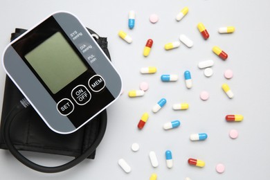 Blood pressure measuring device and pills on light grey background, top view