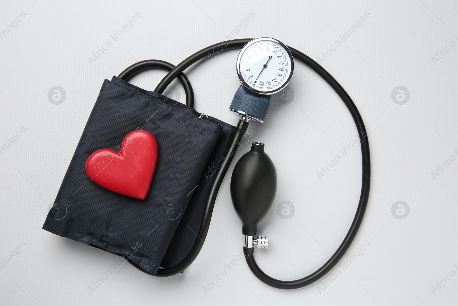 Photo of Blood pressure measuring device and heart figure on light grey background, top view