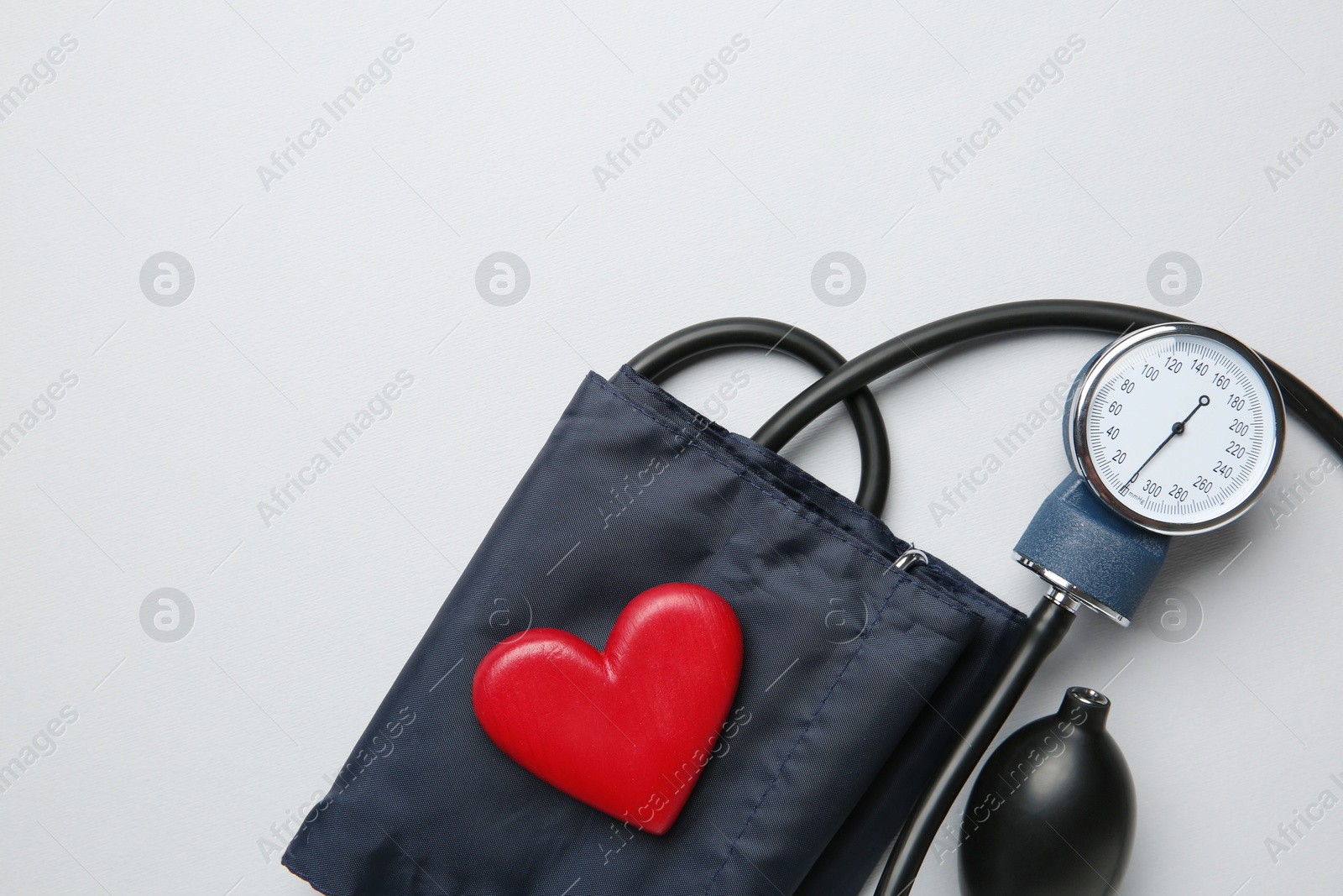 Photo of Blood pressure measuring device and heart figure on light grey background, top view. Space for text