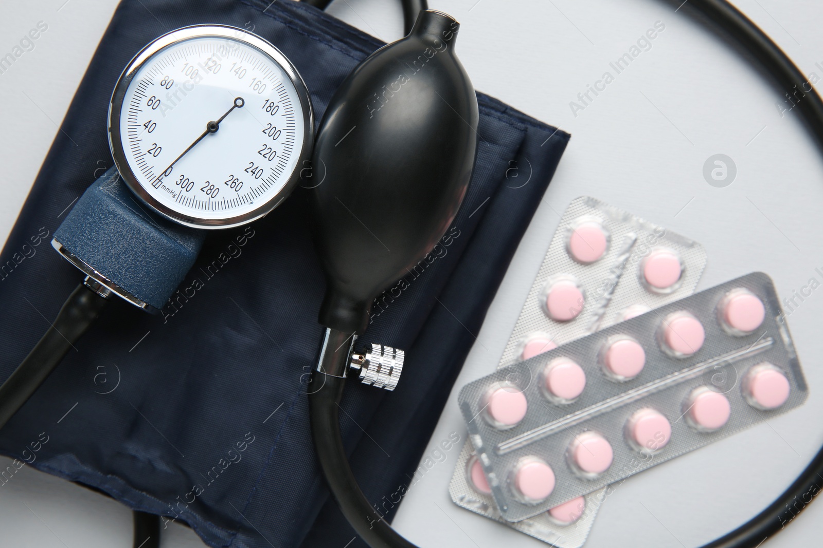 Photo of Blood pressure measuring device and pills on light grey background, top view