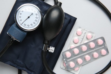 Photo of Blood pressure measuring device and pills on light grey background, top view