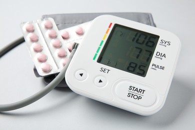 Photo of Blood pressure measuring device and pills on light grey background, closeup