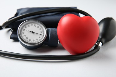 Photo of Blood pressure measuring device and squeeze heart on light grey background, closeup